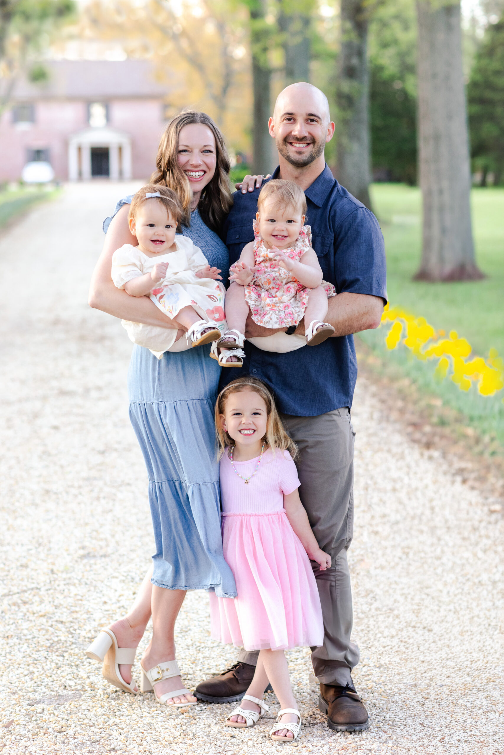 Family photography portrait at Bowlingly Estate on Maryland’s Eastern Shore with parents and three daughters smiling on a tree-lined driveway.